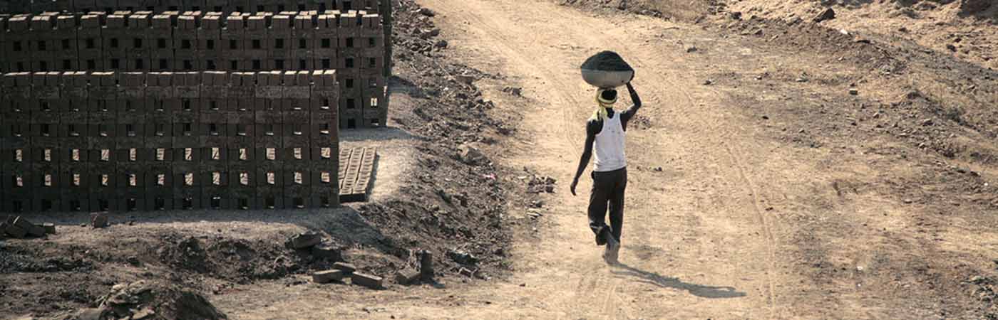 Person walking through dusty land carrying work materials on their head